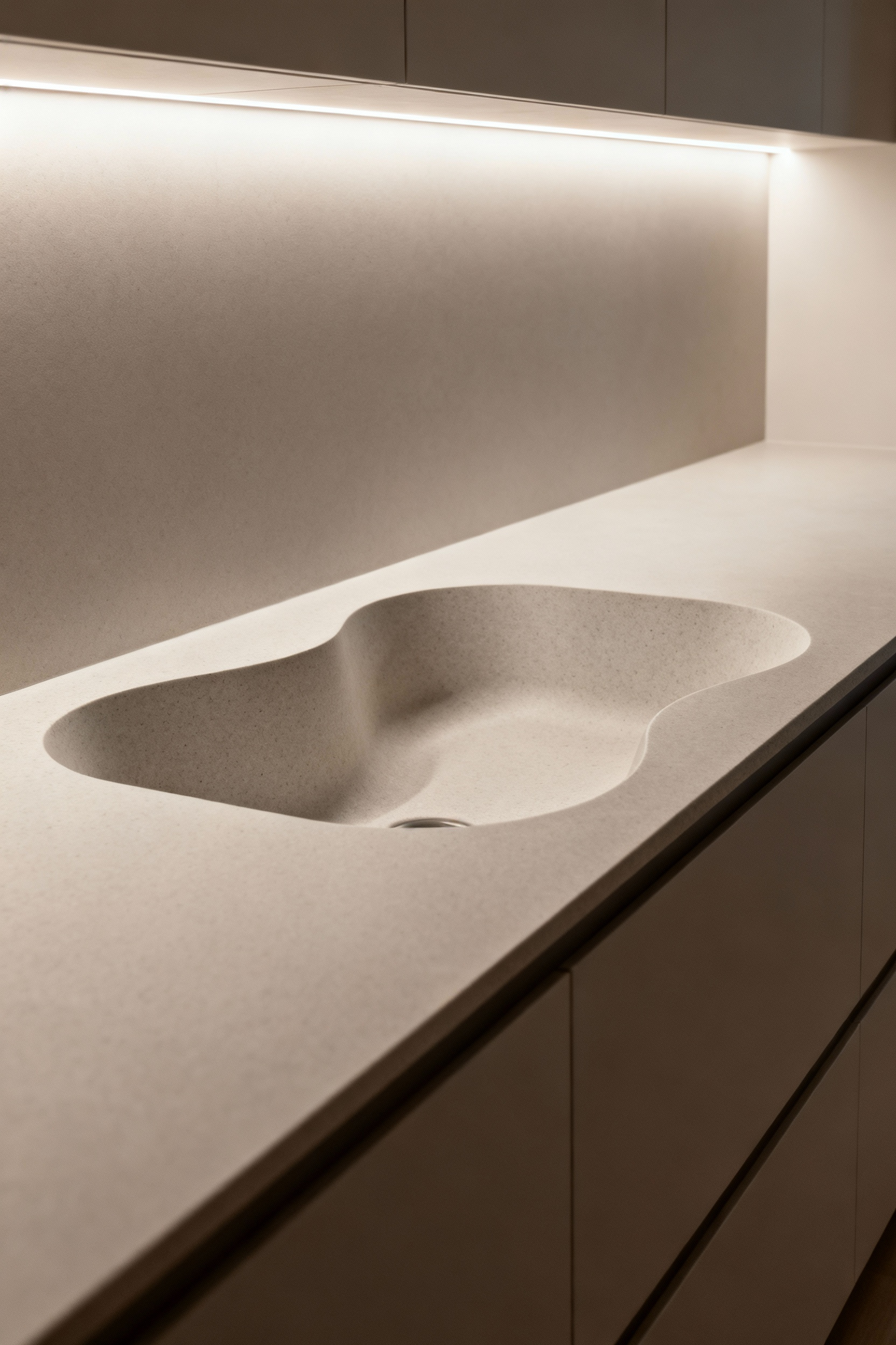 Portrait image of a modern kitchen sink featuring smooth, undulating, and organic lines for visual tranquility and minimalist aesthetic, with integrated LED lighting.