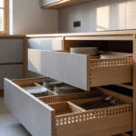 A wide-angle view of a bright Nordic-style kitchen with open pull-out drawers showing organized ash wood dividers and kitchenware.