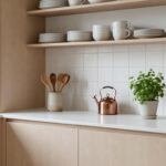 A minimalist, compact Scandinavian apartment kitchen featuring pale wood cabinetry and white tiles, embodying the Swedish Lagom principle with only essential items displayed on the counter.