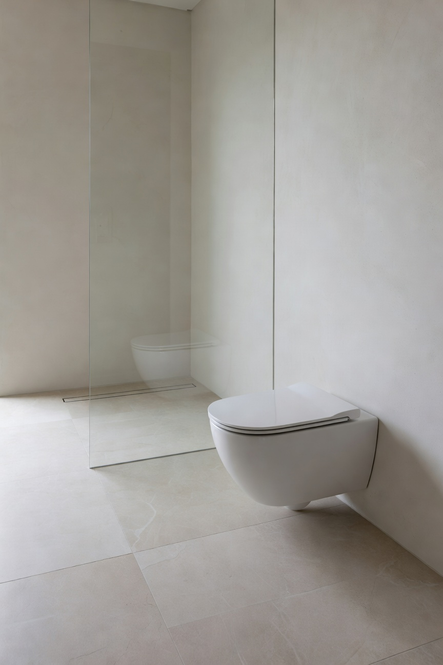 High-end minimalist bathroom renovation with a floating wall-mounted toilet, linear shower drain, and continuous stone tile flooring.