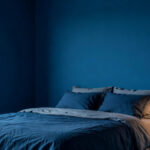 A small bedroom with saturated Nordic blue walls and minimalist furniture designed to demonstrate how dark colors expand a tight space.